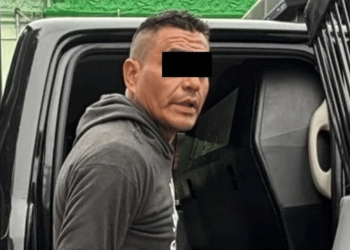 Man in a gray hoodie getting into a dark van or SUV; eyes are covered with a black bar for anonymity.