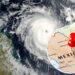 Vista satelital de un huracán frente a la costa mexicana, con un mapa circular insertado de México y una chincheta roja que marca una ubicación cerca de la península de Yucatán.